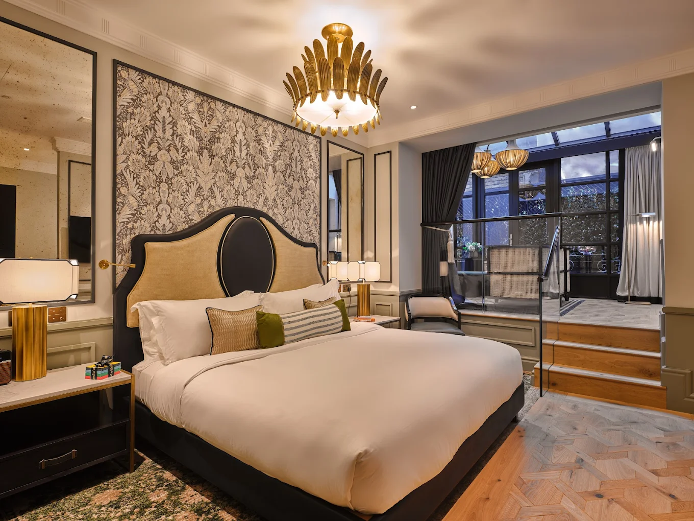 Signature suite at The Mayfair Townhouse featuring a botanical wallpaper feature wall, cane and lacquer headboard, gold chandelier and mezzanine leading to a conservatory