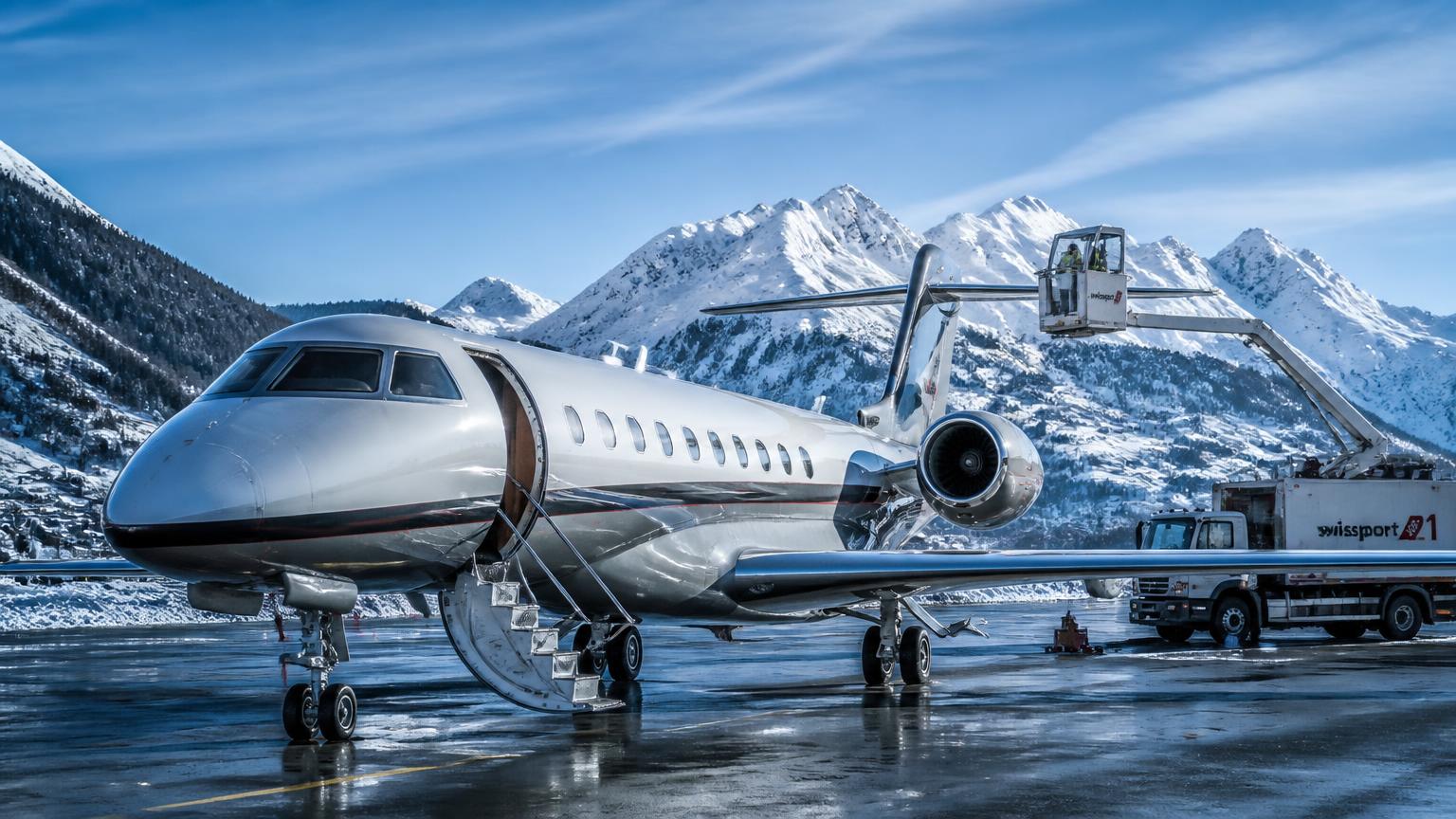 Private jet on a snow-cleared alpine airport apron with de-icing equipment and Swiss mountains behind