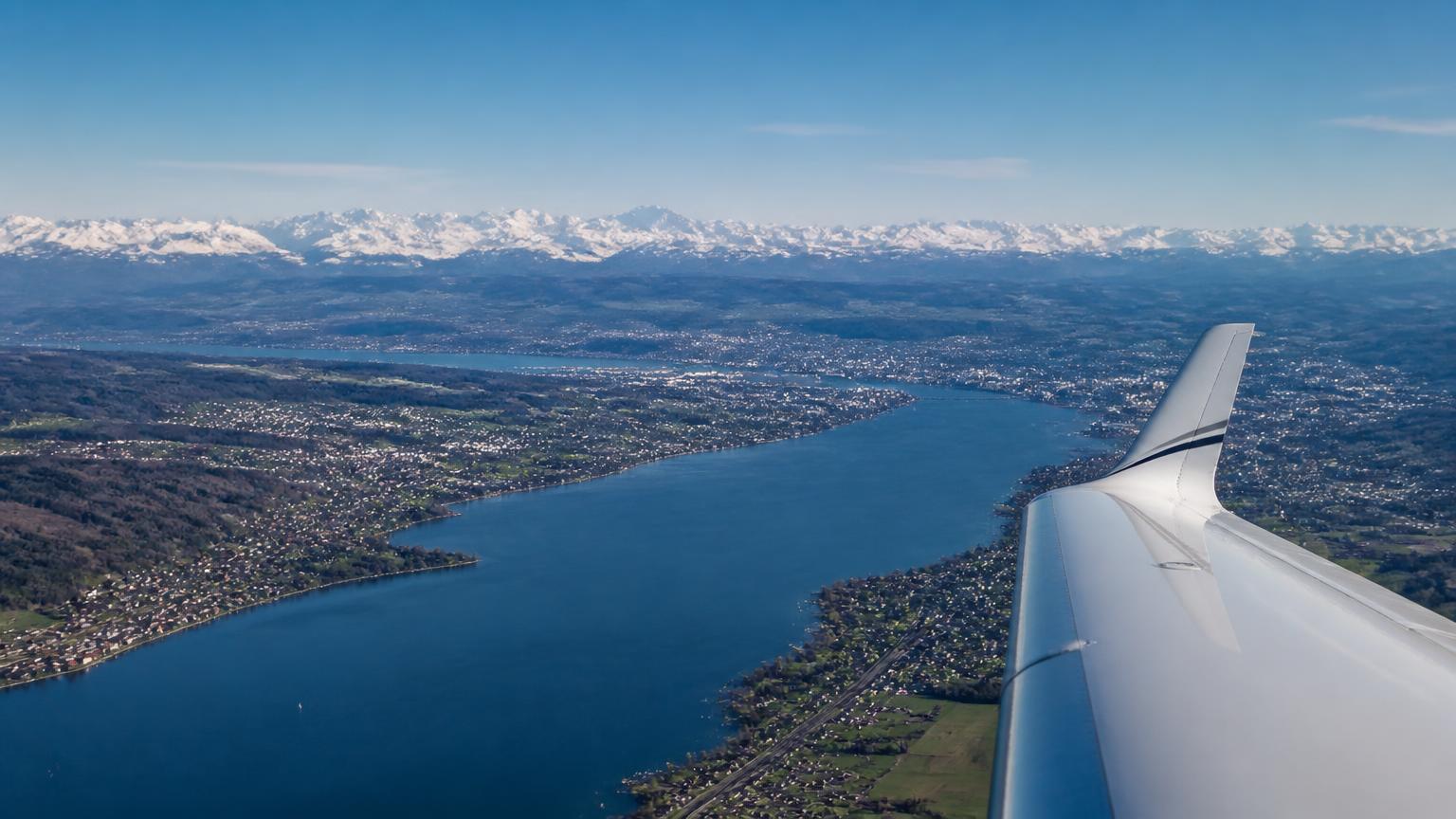 View from a private jet descending over Lake Zurich with the snow-capped Alps in the distance