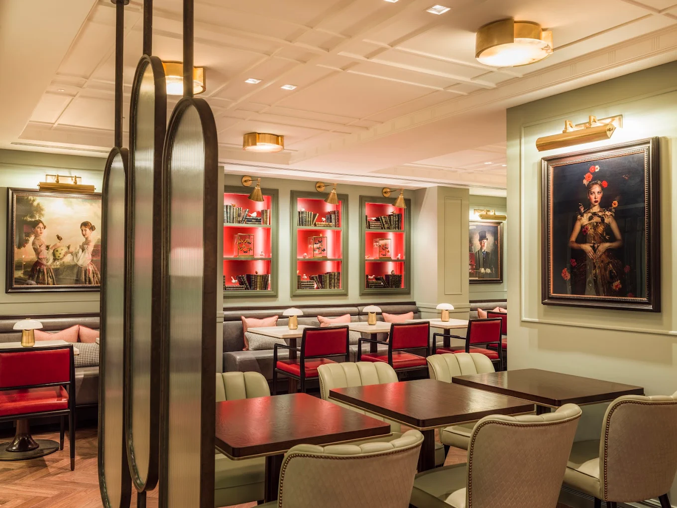 The Dandy Bar at The Mayfair Townhouse — sage-green panelling, coral-lit bookshelves, framed portraits and intimate banquette seating with red and cream chairs