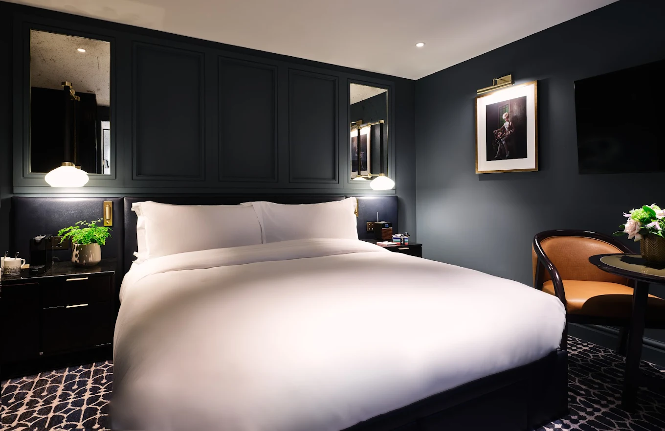 Guest room at The Mayfair Townhouse with dark panelled walls, brass reading lamps, framed portrait art and a crisp white king bed