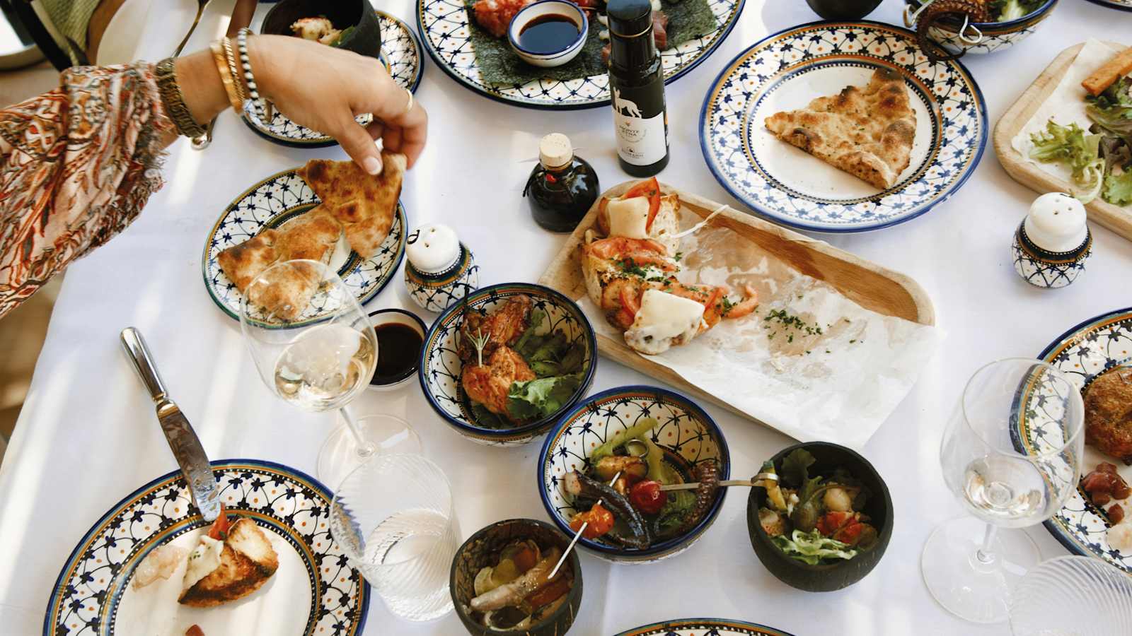 Sicilian dishes shared on a white-linen table at Grand Hotel Timeo — focaccia, tomato and mozzarella crostini, octopus salad and local white wine on painted ceramic plates