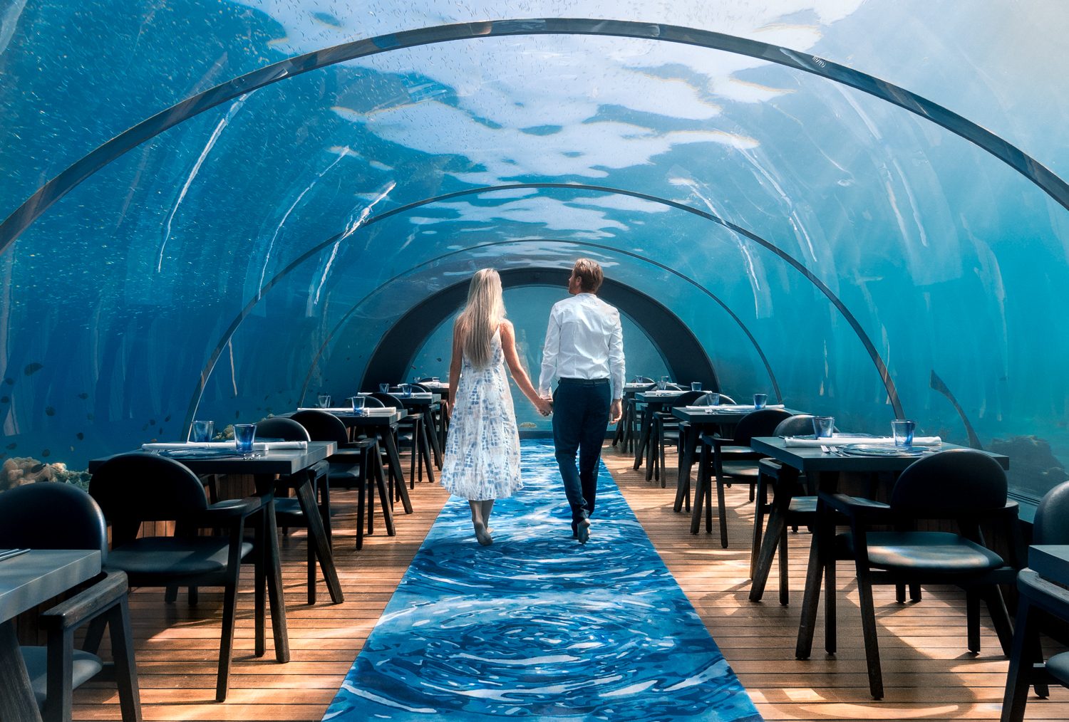 Guests dining in an underwater restaurant surrounded by reef fish in the Maldives
